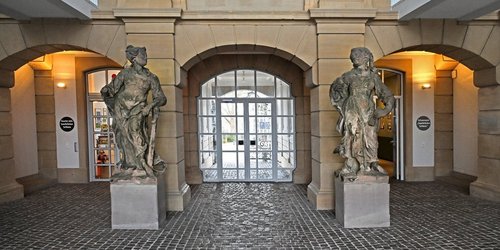 Blick auf zwei braune, leicht verwitterte weibliche Steinskulpturen im Mittelrisalit des Saarbrücker Schlosses.