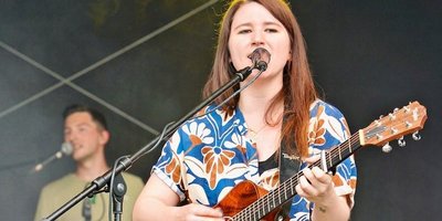 Isabell Krohn steht auf der Bühne mit ihrer Gitarre und singt in ein Mikrofon.