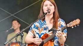 Isabell Krohn steht auf der Bühne mit ihrer Gitarre und singt in ein Mikrofon.
