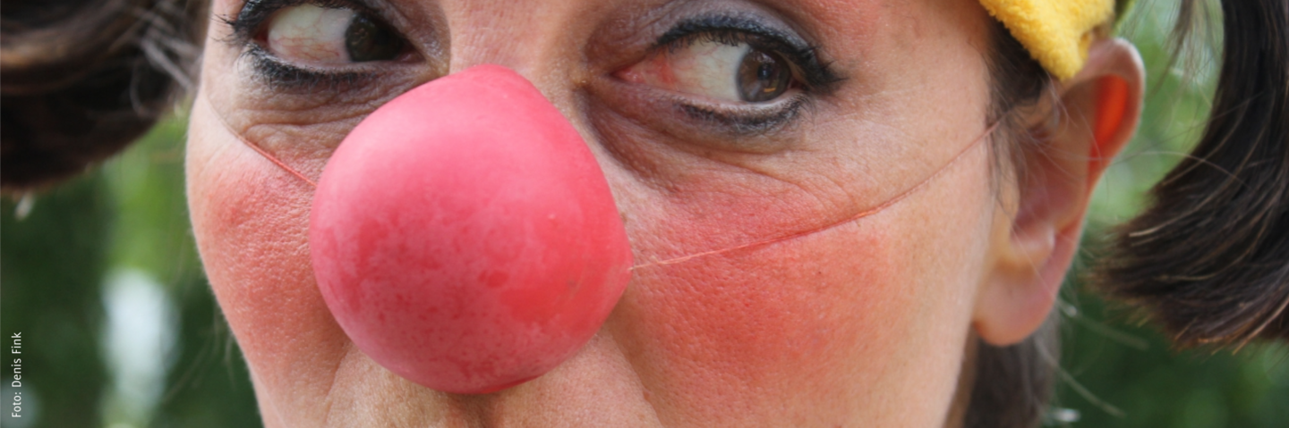 Ein weiblicher Clown mit roter Nase schaut nach links an der Kamera vorbei