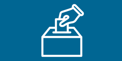 Eine Grafik mit den Worten "Du entscheidest, wer entscheidet" in weißer Schrift auf blauem Hintergrund. Rechts daneben sieht man eine stilisierte Hand, die einen Wahlzettel in eine Wahlurnesteckt. In einem weißen Kasten am oberen Bildrand steht in blauer Schrift "Wahl zur Regionalversammlung am 30. August 2026".