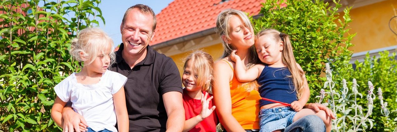 Fünfköpfige Familie vor Wohnhaus sitzend