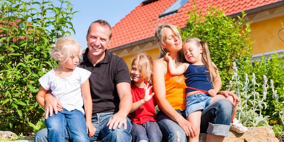 Fünfköpfige Familie vor Wohnhaus sitzend