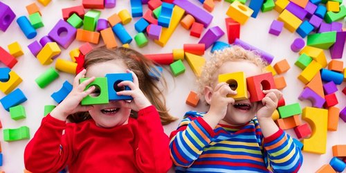 Kleinkinder spielen mit Bauklötzen und halten sich jeweils zwei Bauklötze wie eine Brille vor die Augen