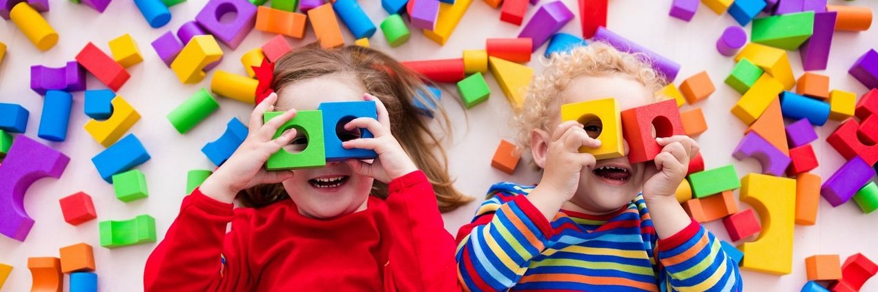 Kleinkinder spielen mit Bauklötzen und halten sich jeweils zwei Bauklötze wie eine Brille vor die Augen