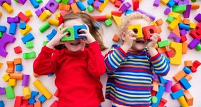 Kleinkinder spielen mit Bauklötzen und halten sich jeweils zwei Bauklötze wie eine Brille vor die Augen