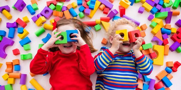 Kleinkinder spielen mit Bauklötzen und halten sich jeweils zwei Bauklötze wie eine Brille vor die Augen