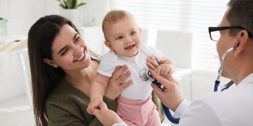 Mutter mit Kind und einem Arzt der das lachende Baby mit einem Stetoskop abhört