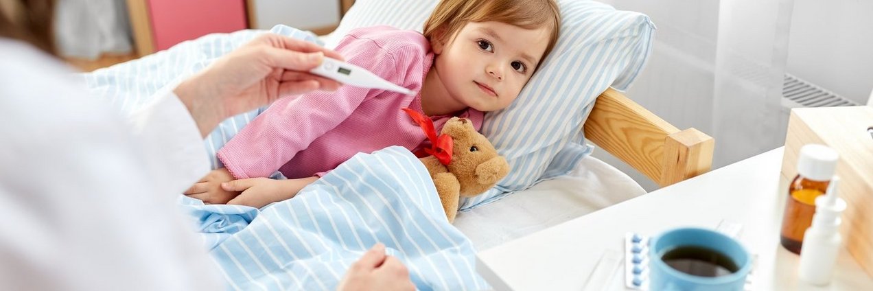 Eine Ärztin misst bei einem kranken Kind Fieber im Bett