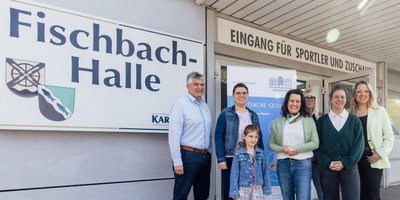Alle nachfolgend benannten Personen stehen vor der Fischbachhalle und lachen in die Kamera: Bürgermeister Lutz Maurer (links) und Regionalverbandsdirektorin Dr. Carolin Lehberger (Mitte) freuten sich gemeinsam mit einer Mutter und ihrem Kind über die soeben erfolgte Schuleingangsuntersuchung in der Fischbachhalle. Rechts davon das Team des Gesundheitsamtes des Regionalverbandes um Kinderärztin Marie-Therese Pawlita (vorne rechts). 