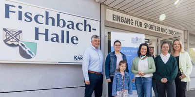 Alle nachfolgend benannten Personen stehen vor der Fischbachhalle und lachen in die Kamera: Bürgermeister Lutz Maurer (links) und Regionalverbandsdirektorin Dr. Carolin Lehberger (Mitte) freuten sich gemeinsam mit einer Mutter und ihrem Kind über die soeben erfolgte Schuleingangsuntersuchung in der Fischbachhalle. Rechts davon das Team des Gesundheitsamtes des Regionalverbandes um Kinderärztin Marie-Therese Pawlita (vorne rechts). 