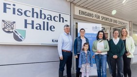 Alle nachfolgend benannten Personen stehen vor der Fischbachhalle und lachen in die Kamera: Bürgermeister Lutz Maurer (links) und Regionalverbandsdirektorin Dr. Carolin Lehberger (Mitte) freuten sich gemeinsam mit einer Mutter und ihrem Kind über die soeben erfolgte Schuleingangsuntersuchung in der Fischbachhalle. Rechts davon das Team des Gesundheitsamtes des Regionalverbandes um Kinderärztin Marie-Therese Pawlita (vorne rechts). 