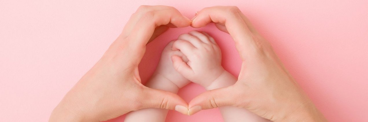 Elternteil hält die Hände in Herzform schützend über Babyhände