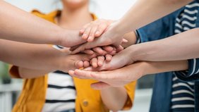 Menschen halten die Hände aufeinander um Zusammenhalt zu demonstrieren