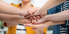 Menschen halten die Hände aufeinander um Zusammenhalt zu demonstrieren