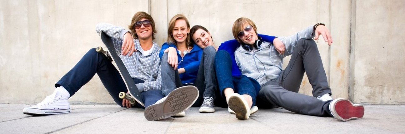 Eine Gruppe Jugendlicher sitzt auf dem Boden und lacht in die Kamera
