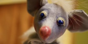 Die Figur einer grauen Maus blickt in die Kamera.