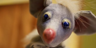 Die Figur einer grauen Maus blickt in die Kamera.