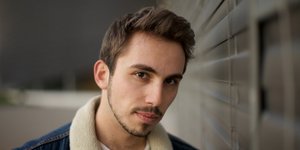 Ein junger Mann mit kurzem braunem Haar und Jeansjacke blickt in die Kamera.