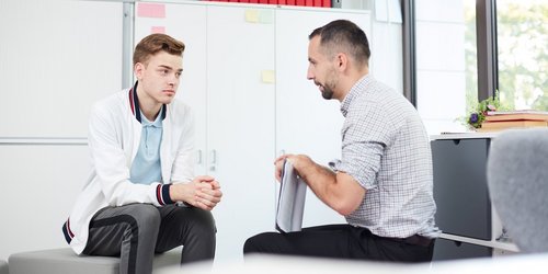 ein Mann sitzt mit einem Jugendlichen in seinem Büro bei einem Gespräch