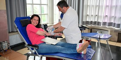 Regionalverbandsdirektorin Dr. Carolin Lehberger auf eine Liege liegend und in die Kamera lächelnd, während sie eine Kanüle zum Blutabnehmen im Arm hat.