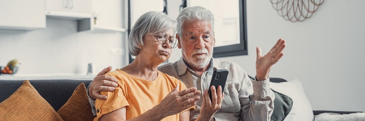 Ein Seniorenpaar schaut geschockt auf das Telefon.