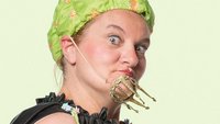 Eine Frau mit grüner Badekappe und schwarzem Umhang hat eine Spielzeugkrone am Kinn befestigt.