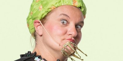 Eine Frau mit grüner Badekappe und schwarzem Umhang hat eine Spielzeugkrone am Kinn befestigt.