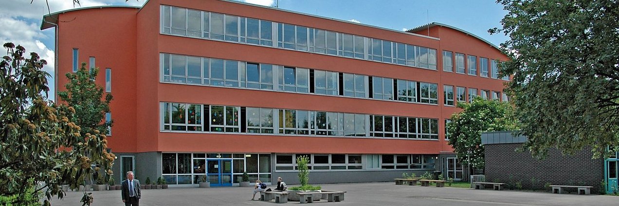 rotes Schulgebäude mit einem großen Schulhof mit Spielgeräten 