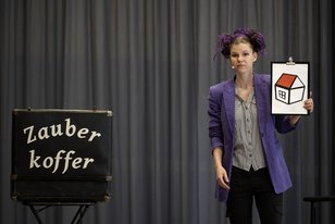 Zauberkünstlerin Lila Lucy mit ihrem Zauberkoffer und einem Bild auf der Bühne