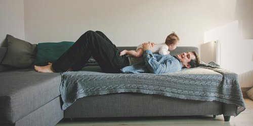 Vater mit Baby im Arm auf dem Sofa