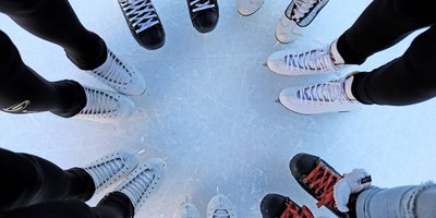 Ein Blick von oben auf einen Kreis aus Fußpaaren in Schlittschuhen auf dem Eis