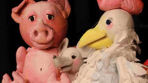 Die Stoffpuppen eine rosafarbenen Schweinchens, einer grauen Maus und eines weißen Hahns mit rotem Kamm sitzen nebeneinander.
