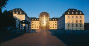 Blick auf das Saarbrücker Schloss mit Vorplatz. In der Glasfront spiegelt sich die untergehende Sonne