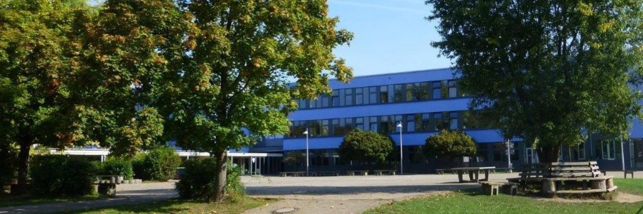 Ansicht des Schulgebäudes in Heusweiler mit begrüntem Schulhof und Sitzgelegenheiten.