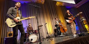 Isabell Krohn tritt gemeinsam mit den drei Mitgliedern ihrer Band "The Strangers" auf der Bühne des Festsaals auf. Die drei Männer spielen Gitarre, Schlagzeug und Bass, Isabell Krohn Gitarre.