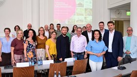 Eine Gruppe vor einer Projektion mit der Aufschrift "Fortschreibung Tourismusstrategie Region Saarbrücken 2030 lächelt im Sitzungssaal des Saarbrücker Rathauses in die Kamera