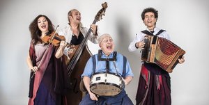 Drei Männer und eine Frau in starker Schminke und bunter Kleidung spielen enthusiastisch auf ihren Instrumenten.