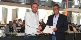 Der frisch gewählte neue Ehrenamtliche Beigeordnete Patrick Ginsbach (l.) nimmt die Urkunde und die Glückwünsche von Regionalverbandsdirektor Peter Gillo entgegen. Foto: Stephan Hett/Regionalverband