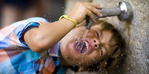 Junge trinkt Wasser aus Wasserhahn an einem Trinkbrunnen