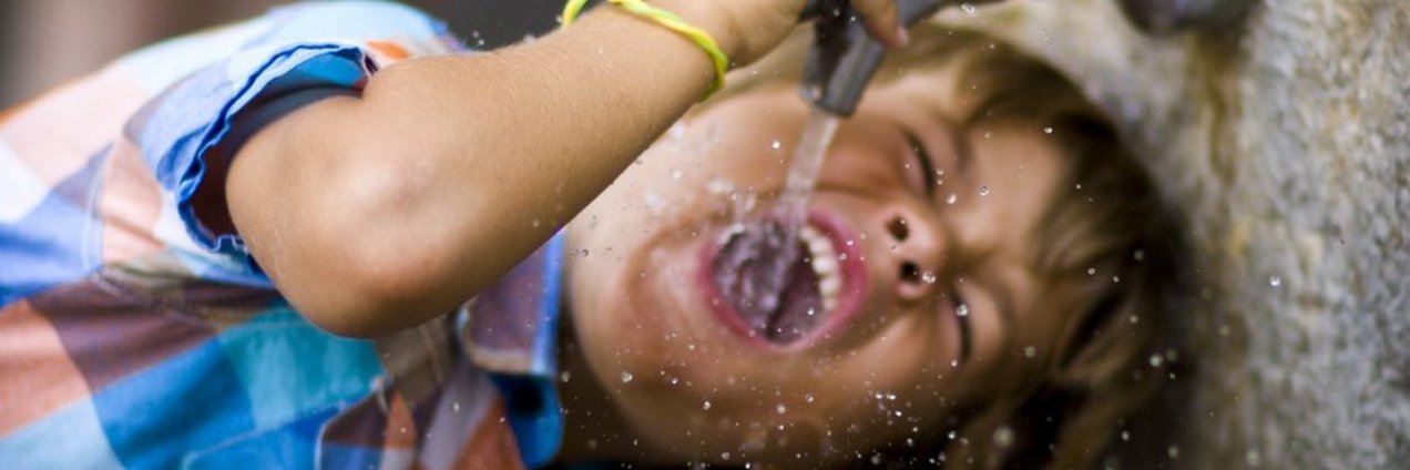 Junge trinkt Wasser aus Wasserhahn an einem Trinkbrunnen