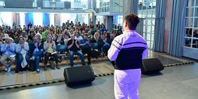 Blick von der Bühne im Festsaal des Saarbrücker Schlosses in das Publikum. Die Menschen in den Sitzreihen klatschen. Von hinten ist ein junge auf der Bühne zu sehen, der einen Rap vorträgt.