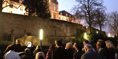 Gruppe Menschen steht im halb dunkeln vor Schlossmauer im Schlossgarten 