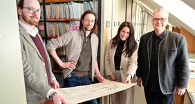 Regionalverbandsdirektorin Dr. Carolin Lehberger (2.v.r.) und UBA-Leiterin Uta Pitz gemeinsam mit Projektmanager Daniel Bitz (l.) und UBA-Mitarbeiter Alexander Stein im Archiv im Saarbrücker Schloss. Alle halten einen roßen Bauplan in der Hand und lächeln in die Kamera.
