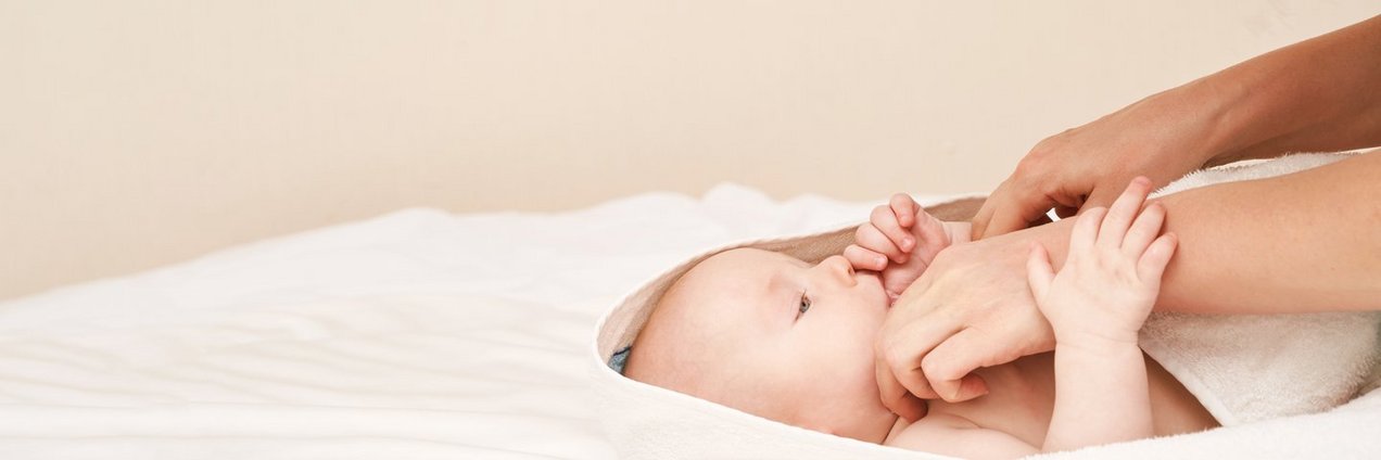 Blick von der Seite auf ein Neugeborenes welches nach einer Frauenhand greift - heller Hintergrund und helles Handtuch 