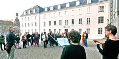 Menschengruppe mit Führer vorm Schloss, zwei Musikerinnen spielen Musik 