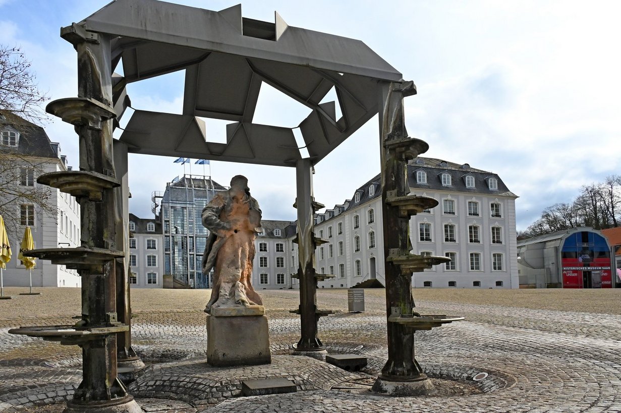 eine dunkelgraue, überdachte und auf vier Säulen stehende Brunnenanlage am Schlossplatz. In der Mitte eine fragmentarisch erhaltene Steinskulptur des Apostels Paulus. 