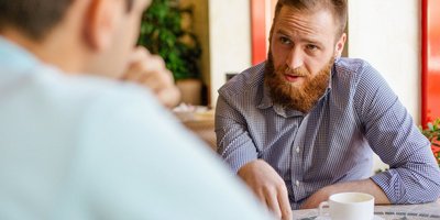 Berufsbetreuer Blick über die Schuler eines Mannes, der am Tisch sitzt und mit einem jungen Mann ein Gespräch führt
