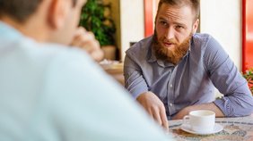 Berufsbetreuer Blick über die Schuler eines Mannes, der am Tisch sitzt und mit einem jungen Mann ein Gespräch führt