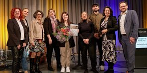 Die Jurymitglieder des Kulturpreises für Musik 2025 posieren mit der Preisträgerin Isabell Krohn und Regionalverbandsdirektorin Dr. Carolin Lehberger auf der Bühne des Festsaals für ein Foto. Isabell Krohn hält ihre Urkunde und einen Blumenstrauß.
